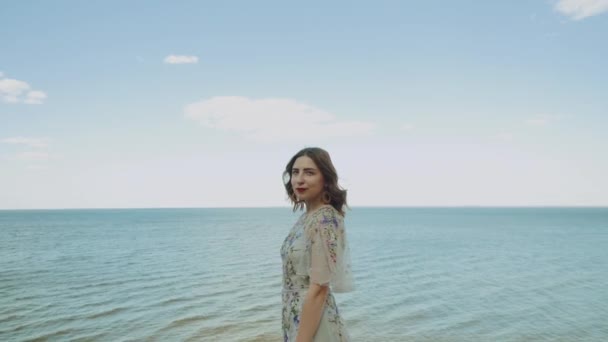 Μια γυναίκα κοιτάζει την κάμερα και η θάλασσα και τα άσπρα σύννεφα ενώνονται με το νερό στον ορίζοντα στο βάθος. Μέτριο πλάνο. — Αρχείο Βίντεο
