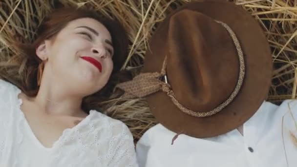 Beautiful red-haired Caucasian women in white dress on field of spikelets posing, smiling, the girl takes the brown hat from the guy and indulges. — Stock video