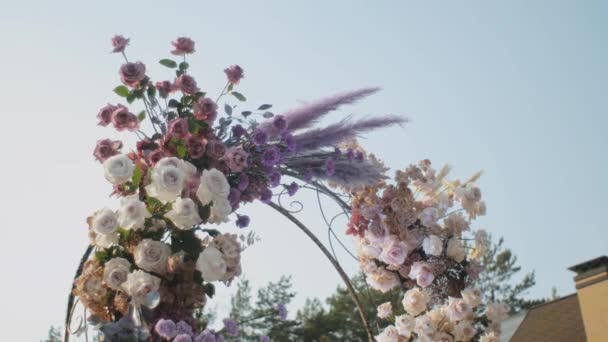 Vista de plano medio de la boda decoraciones florales de flores en colores pastel descoloridos cámara lenta, fuera de la ceremonia de la boda en el parque, los rayos del sol brillan a través del arco. — Vídeos de Stock