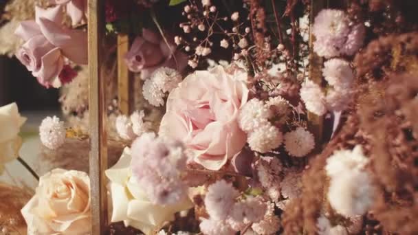 Vista de cerca de la boda decoraciones florales de flores en colores pastel descoloridos cámara lenta, fuera de la ceremonia de la boda en el parque, los rayos del sol brillan a través del arco. — Vídeos de Stock