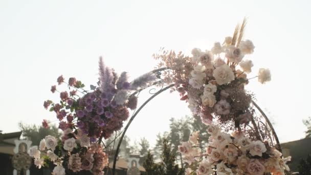 Medium shot view of Wedding floral decorations of flowers in pastel faded colors slow motion, outside wedding ceremony in park, the suns rays shine through the arch. — Stock Video