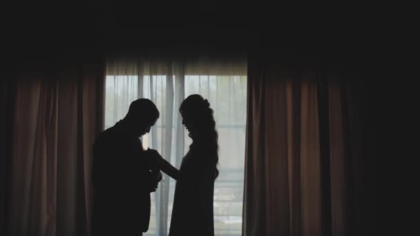 Egy friss házas, szerető pár sziluettje áll az ablak mellett. A menyasszony hozzáér a vőlegényhez, és leül egy padra a régi házban. — Stock videók