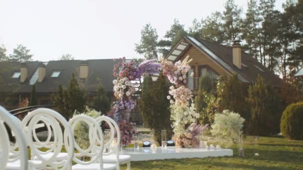 Άποψη του γάμου floral διακοσμήσεις λουλουδιών σε παστέλ ξεθωριασμένα χρώματα αργή κίνηση, έξω γαμήλια τελετή στο πάρκο, οι ακτίνες του ήλιου λάμπουν μέσα από την αψίδα. — Αρχείο Βίντεο