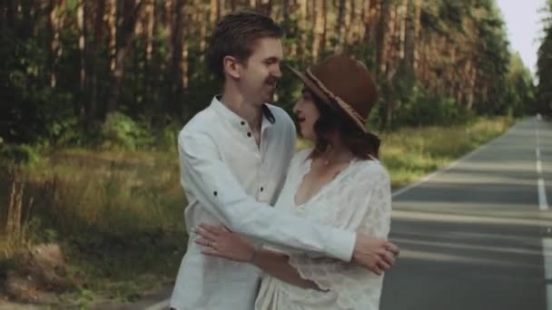 A cheerful young European couple is walking in a picturesque place in the pine forest, with soft natural lighting. Couple kissing and hugging, holding hands, couple kissing and hugging . slow motion — Vídeo de Stock