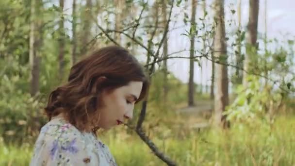 Aantrekkelijke vrouw met rode lippen raakt haar krullend haar lopen in het bos slow motion. blauwe zee met golven en blauwe lucht op de achtergrond. — Stockvideo