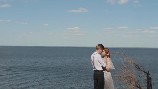 Par i kärlek kramar, paret står mitt emot varandra med slutna ögon, havet är i bakgrunden, vinden utvecklar kvinnligt hår. — Stockvideo