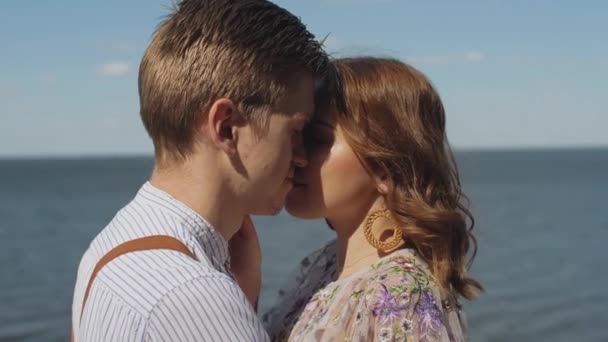 Couple in love hugs, medium shot the couple stands opposite each other with their eyes closed, slow motion, the sea is in the background, the wind develops female hair. — Wideo stockowe