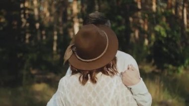 Neşeli genç Avrupalı bir çift, çam ormanında yumuşak doğal ışıklandırmayla pitoresk bir yerde yürüyor. Çift öpüşüyor, sarılıyor, el ele tutuşuyor, çift öpüşüyor ve sarılıyor. yavaş çekim 