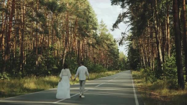 Aşık hippi çift güzel bir yerde yürür, el ele tutuşur, kadın ve erkek, boş yolda pikoresk çam ormanlarında sarılır ve eğlenir. yavaş çekim — Stok video
