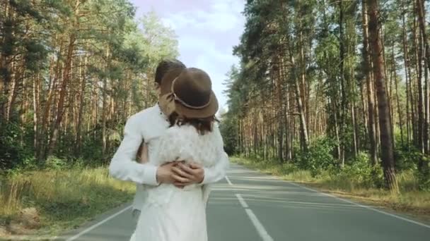 Hipster szerelmespár séta gyönyörű helyen, kéz a kézben, férfi és nő ölelés és élvezi együtt az üres úton keresztül festői fenyőerdő. lassított felvétel — Stock videók