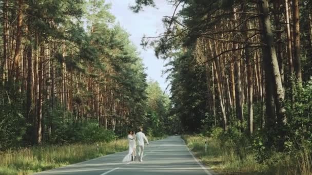 Hipster couple in love walk in beautiful place, hold hands, man and woman hugging and enjoying togetherness on empty road across picturesque pine forest. slow motion — Vídeo de Stock