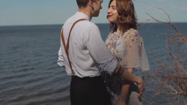 The guy comes up to the girl, hugs and strokes her hair, the girl smiles at him slow motion. Close-up of couple in love hugs, the sea is in the background. — ストック動画