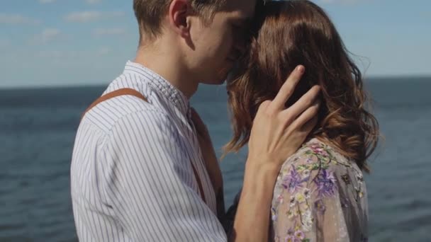 Primer plano de la pareja en abrazos de amor, la pareja se coloca uno frente al otro con los ojos cerrados, cámara lenta, el mar está en el fondo, el viento desarrolla el cabello femenino. — Vídeo de stock