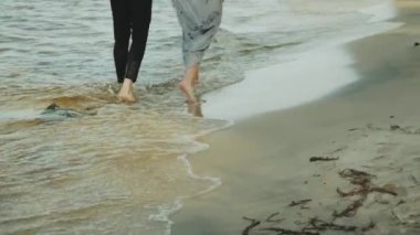 Sahilde birlikte yürüyen mutlu çift harika ve çok romantik, ayaklarına yakın, suda ağır çekimde yürüyorlar.