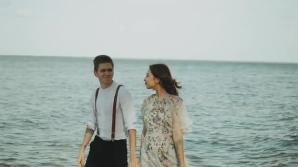 Sahilde birlikte yürüyen mutlu çift harika ve çok romantik hissediyorlar, el ele tutuşuyorlar ve ayakları su üzerinde yürüyorlar, ağır çekimde. — Stok video