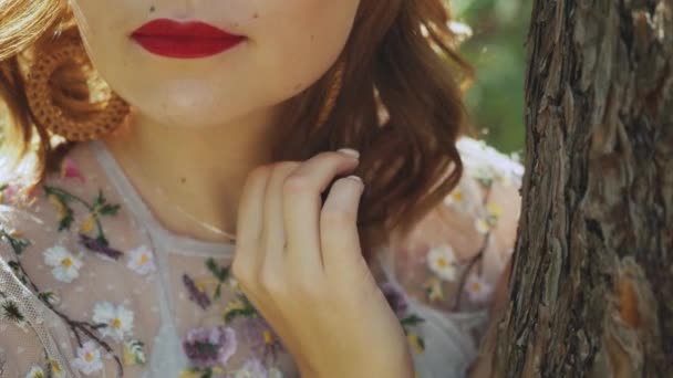 Zbliżenie piękne kobiety usta z czerwoną szminką, curling jej włosy stojące w pobliżu drzewa. — Wideo stockowe