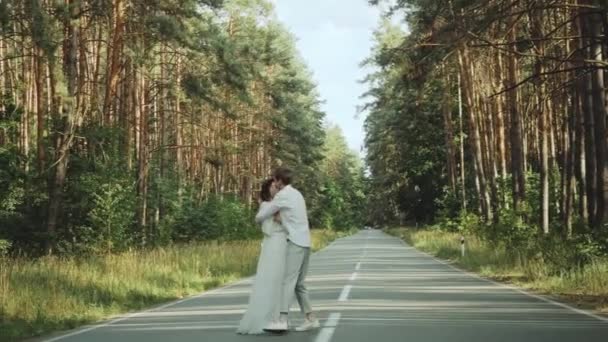 美しい場所での愛の散歩でヒップスターカップルは、手を握り、男と女が抱き合って、絵のように松の森を渡って空の道で一緒に楽しむ。スローモーション — ストック動画