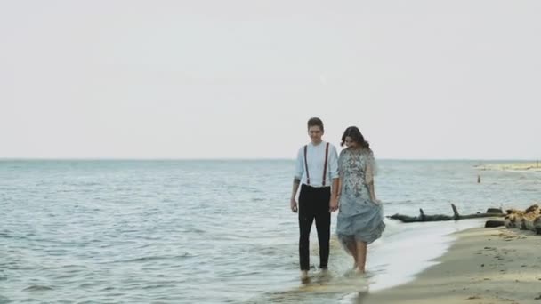 Sahilde birlikte yürüyen mutlu çift harika ve çok romantik hissediyorlar, el ele tutuşuyorlar ve ayaklarıyla suda ağır çekimde yürüyorlar. — Stok video