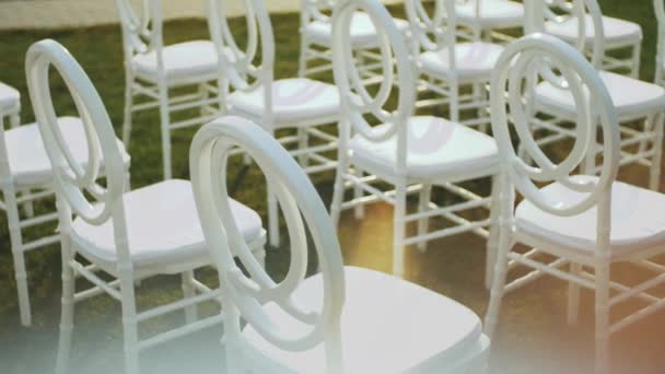 Λευκές καρέκλες για τους καλεσμένους σε μια γαμήλια τελετή αργή κίνηση. Εξερχόμενη τελετή γάμου στον κήπο. Διακόσμηση, καρέκλες για την γαμήλια τελετή στο γκαζόν. — Αρχείο Βίντεο
