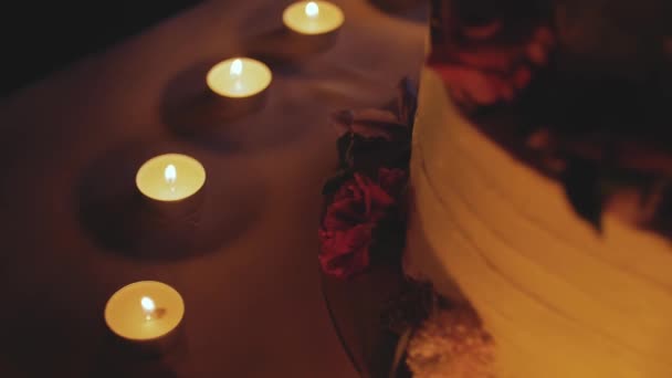 Grande bolo de casamento bonito decorado com flores à noite perto do arco close-up, câmera lenta. velas no fundo. — Vídeo de Stock