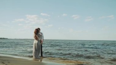 Sahilde kucaklaşan mutlu çift harika ve çok romantik hissediyor, dalgalar ayaklarına çarpıyor, el ele tutuşuyorlar ve suda ayaklarıyla yürüyorlar. Yüksek kalite 4k görüntü