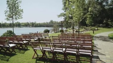 Düğün kemeri ve ahşap sandalyeler arka planda güzel nehir, yavaş çekim. Parkta yaz düğünü. Çiçeklerle süslenmiş ahşap kemer. Yüksek kaliteli FullHD görüntüler