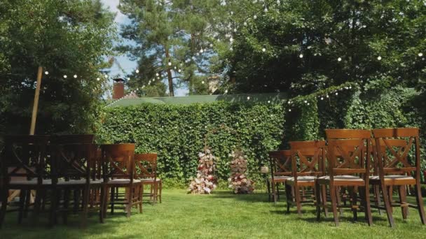公園のスローモーションショットでパステル調の色あせた花や木製の椅子で飾られた雑草のアーチ ボヘミアンシックな結婚式スタイル 高品質のフルHd映像 — ストック動画
