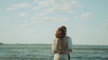 Sahilde kucaklaşan mutlu bir çift harika ve çok romantik hissediyorlar, el ele tutuşuyorlar ve ayakları suyun üzerinde yürüyorlar. Yüksek kalite 4k görüntü