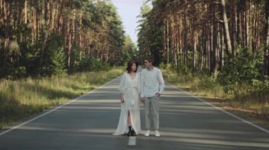Güzel bir çift yolun ortasında el ele tutuşup kameraya bakar. Ormanın içinden geçen yol, güneşli hava. Yüksek kalite 4k görüntü