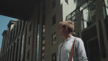 Man looking to camera while standing outdoors business building on the background. Medium shot Portrait of male person dressed in stylish clothes. High quality 4k footage