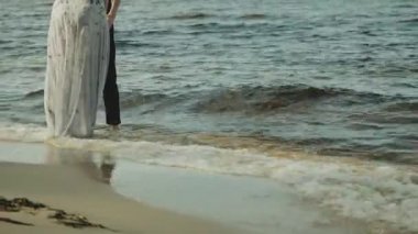 Sahilde kucaklaşan mutlu çift harika ve çok romantik hissediyorlar. Dalgalar ayaklarına çarpıyor, el ele tutuşuyorlar ve suda yürüyorlar. Yüksek kalite 4k görüntü