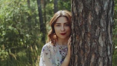 Ağaç kabuğunun yanındaki ormanda poz veren güzel beyaz kadın portresi, tutuş açısı, ağaç dalları arasından görüntü. Yüksek kalite 4k görüntü