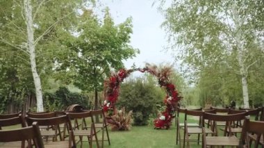 Parktaki ağır çekimde kırmızı kemer ve tahta sandalyeler. Boho-şık düğün tarzı. Yüksek kaliteli FullHD görüntüler