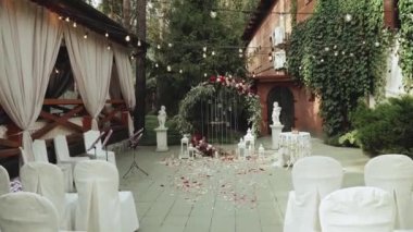 Kırmızı çiçekli düğün kemeri ve beyaz sandalyeler, restoranın yakınındaki törenin üzerine lamba çelengi. Boho-şık düğün tarzı. Yüksek kaliteli FullHD görüntüler