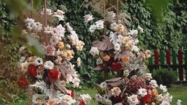Close-up wedding arch decorated with pastel faded flowers and wooden chairs in the park slow motion shot. Boho-chic wedding style. High quality FullHD footage