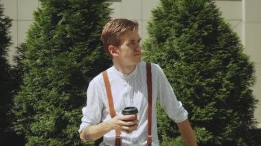 Bir fincan kahveyle bir adamın portresi, şık kıyafetler giymiş biri, ağır çekimde. Adam arka planda iş binasında dikilirken kameraya bakıyor. 4k görüntü