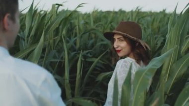 Beautiful couple in the corn field. slow motion. Follow me shot of young woman in brown hat pulling her boyfriend across cornfield. Love and happiness concept. High quality 4k footage