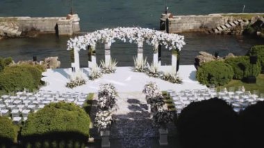Wedding arch decorated with pastel faded flowers and white chairs lake on the background, slow motion shot. Rustic wedding. High quality FullHD footage