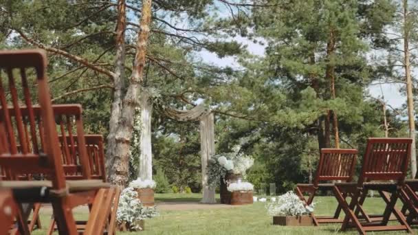 公園のスローモーションショットでパステル調の色あせた花や木製の椅子で飾られた雑草のアーチ 素朴な結婚式のスタイル 高品質のフルHd映像 — ストック動画