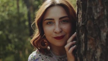 Ağaç kabuğunun yanındaki ormanda poz veren güzel beyaz kadın portresi, tutuş açısı, ağaç dalları arasından görüntü. Yüksek kalite 4k görüntü