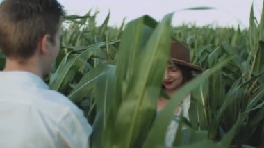 Mısır tarlasında güzel bir çift. Ağır çekim. Kahverengi şapkalı genç bir kadının erkek arkadaşını mısır tarlasında çekerken beni takip edin. Aşk ve mutluluk kavramı. Yüksek kalite 4k görüntü