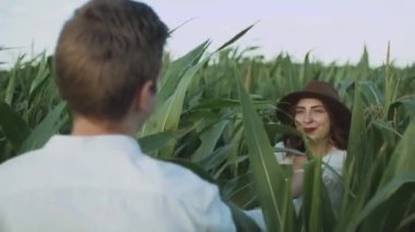 Mısır tarlasında güzel bir çift. Ağır çekim. Kahverengi şapkalı genç bir kadının erkek arkadaşını mısır tarlasında çekerken beni takip edin. Aşk ve mutluluk kavramı. Yüksek kalite 4k görüntü