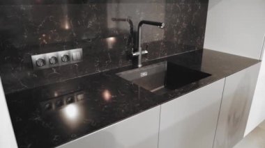 Kitchen sink and faucet. Simple well designed modern kitchen interior. Black ceramic tiles on the wall and countertop, slow motion shot. High quality 4k footage