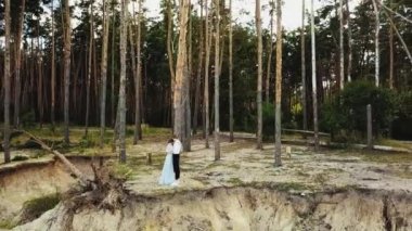 Uçurumun kenarında birbirine aşık bir çift sarılıyor, çift gözleri kapalı, arka planda çam ormanı var. Yüksek kalite 4k görüntü