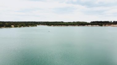 Aerial view of small island with pine trees in the middle of the lake.Unrecognizable people in a boat in the middle of the lake. Close-up shot of island. High quality 4k footage