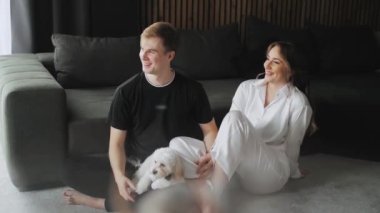 A Lovely Couple with dog sitting on the floor, spouses enjoying of each other. Near a couple a cute dog maltipoo. Happy Young Married Couple Talking. High quality 4k footage