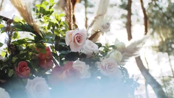 パステルカラーの花の結婚式のアーチの装飾のクローズアップビュースローモーション 松と公園での結婚式の外で 太陽の光はアーチを通して輝きます フルHd映像 — ストック動画