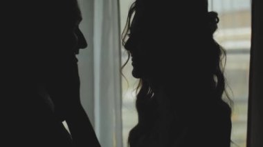 Birbirlerine aşık bir kadın ve erkeğin silueti pencerede öpüşüyorlar. Yeni evli çiftin siluetini orta boy vurdu. Evlilik, romantik bir ortam. Yüksek kaliteli FullHD görüntüler
