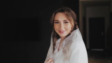 Gelin portresi duvağın altında. Kız peçesine dokunuyor. Törenden önce düğün sabahı hazırlıkları. Kameraya bakan sarı saçlı güzel gelin. Ağır çekim. 4k görüntü