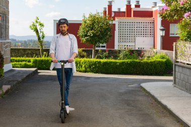 Sokakta elektrikli bir scooter 'ın üzerinde günlük giysiler içinde duran genç bir adam.